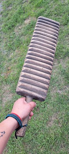 a person holding an old wooden object in their hand with grass and dirt on the ground