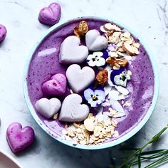 a bowl filled with purple smoothie topped with heart shaped marshmallows and flowers