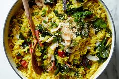 a bowl filled with rice and vegetables on top of a table next to a wooden spoon