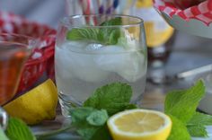 a glass filled with ice, lemon and mint next to other drinks on a table