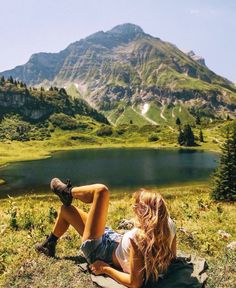 a woman sitting on top of a grass covered field next to a large mountain range