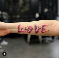 a person's arm with the word love written on it and watercolor splatters