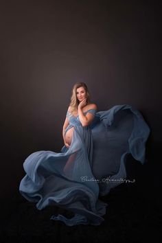 a pregnant woman in a blue dress poses for a studio portrait with her hands on her belly