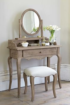 a vanity with a mirror and stool in a room next to a wall, flowers on the table