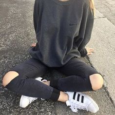 a woman sitting on the ground with her legs crossed wearing black jeans and white sneakers