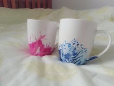 two coffee mugs sitting on top of a bed covered in white and pink paint