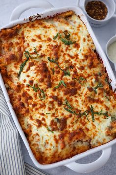 a casserole dish with meat and cheese in it on a striped cloth next to bowls of sauces