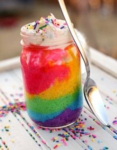 there is a spoon that is next to a jar with colored liquid in it and sprinkles on the table