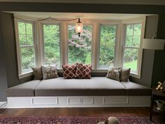 a window seat with pillows on top of it in front of a rug and lamp