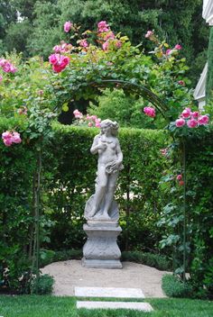 a statue in the middle of a garden with pink roses around it and an archway