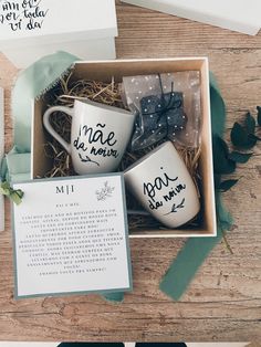 three coffee mugs in a gift box on a table with some cards and flowers