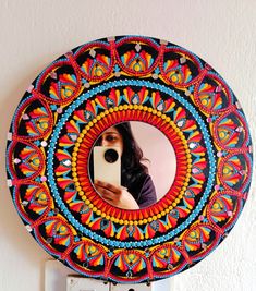 a woman taking a selfie with her phone in front of a colorful circular mirror