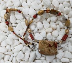 The centerpiece of this necklace is a beautiful yellow-brown and rust colored jasper shield, which is 1 1/2 inches wide by 1 1/4 inches high. I used beads to pull out the autumn hues of the stone centerpiece, with multiple rusts and yellow-browns. The beads include red jasper, picture jasper, Indonesian petrified coral, cultured pearls, Czech glass, and Swarovski crystal. I also bordered the stone centerpiece with sterling silver beads, and used multiple sterling spacer beads and larger sterling accent beads to add sparkle to the necklace.  The hook and loop style clasp is sterling silver. The necklace is 20 1/2 inches long, and will go great with casual and more formal attire. There are also matching earrings available, that include red jasper, picture jasper, Swarovski crystal, and sterl Earthy Brown Beaded Necklaces With Gemstones, Brown Jasper Necklaces For Jewelry Making, Brown Jasper Beaded Necklace For Gift, Brown Jasper Necklaces For Healing, Earthy Brown Beaded Gemstone Necklaces, Brown Jasper Necklaces As Gifts, Brown Jasper Necklace With Gemstone Beads, Brown Jasper Necklace With Natural Stones, Brown Jasper Gemstone Bead Necklaces