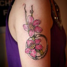 a woman's arm with pink flowers and a circle tattoo on the left shoulder