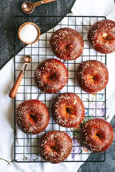 bagels with sesame seeds and sprinkles sit on a cooling rack next to a spoon