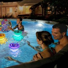 three people are in the pool playing with balls and water toys while another man watches