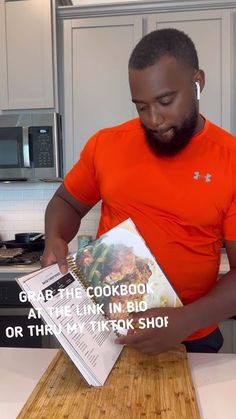 a man in an orange shirt is holding a cookbook and looking down at it