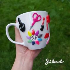 a hand holding a white coffee cup decorated with scissors and paintbrushes on it