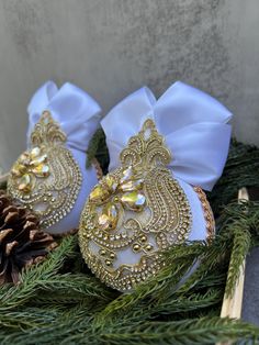 two white and gold christmas ornaments sitting on top of pine cones