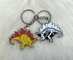 two dinosaur shaped key chains sitting on top of a white fur covered floor next to each other