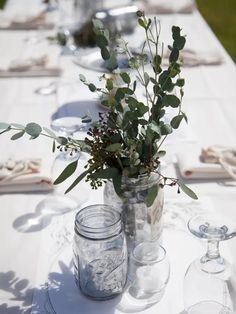 the table is set with mason jars and glass vases filled with greenery on it