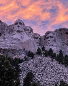 some very large statues on the side of a mountain with trees in front of them