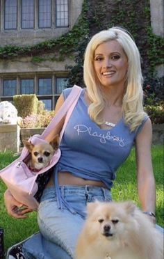 a woman sitting on the grass with two dogs in her lap and one is holding a pink purse