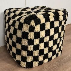 a black and white checkered ottoman sitting on top of a wooden floor next to a wall