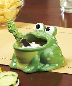 a green frog sitting on top of a wooden table next to sliced cucumbers