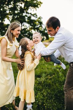 a man is holding a baby and two other people are standing in the grass together