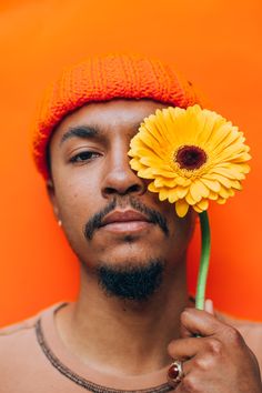 a man holding a yellow flower in front of his face with an orange hat on