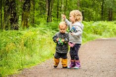 two young children standing on a dirt road in the woods