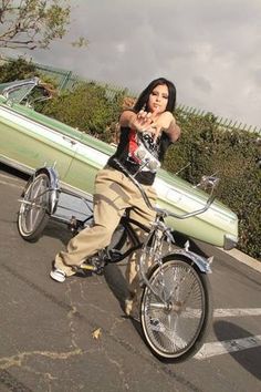 a woman riding on the back of a bike in a parking lot next to a green car