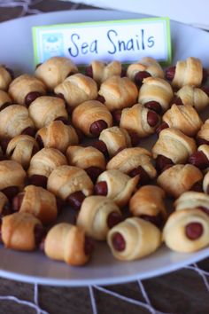 small hotdogs wrapped in crescented bread are on a plate next to a sign that says sea snails