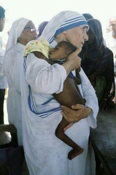 an old woman holding a baby in her arms while other people stand around and watch