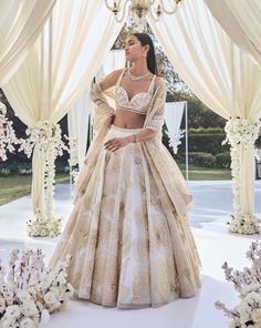 a woman in a white and gold wedding dress standing next to a chandelier