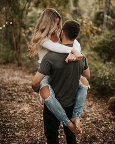 a man holding a woman in his arms while she is walking through the woods with her back to him