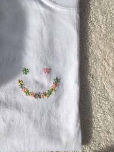 a white t - shirt with a smiley face made out of flowers on the front