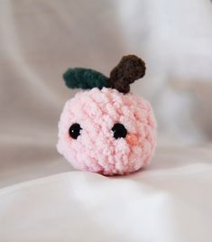 a small pink stuffed animal with a leaf on its head sitting on a white sheet