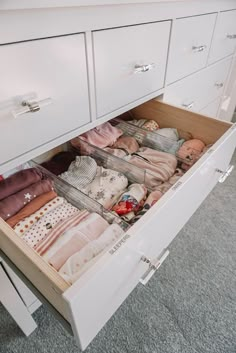 an open drawer with clothes in it on carpeted floor next to white cabinet doors