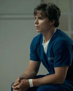 a young man sitting on the floor with his hands folded and looking off to the side