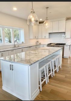 a large kitchen with white cabinets and marble counter tops on the island in front of an oven