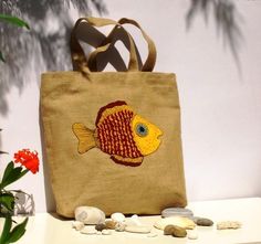 a brown bag with a fish on it sitting next to some rocks and flowers in front of a white wall