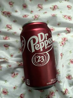 a can of soda sitting on top of a bed covered in pink flowers and white sheets