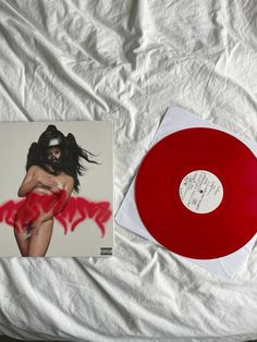 a red vinyl record sitting on top of a bed next to a white sheet covered wall