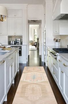 a large kitchen with white cabinets and wood flooring, along with an area rug