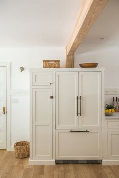 a white kitchen with wooden floors and cabinets in the corner, along with a basket on top of the cupboards