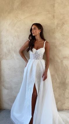 a woman standing in front of a wall wearing a white dress and high slit skirt