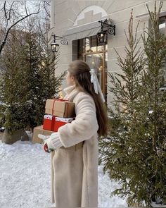 a woman carrying boxes in the snow near a building with christmas trees and lights on it