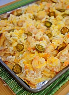 a casserole dish with shrimp, cheese and olives on a green mat